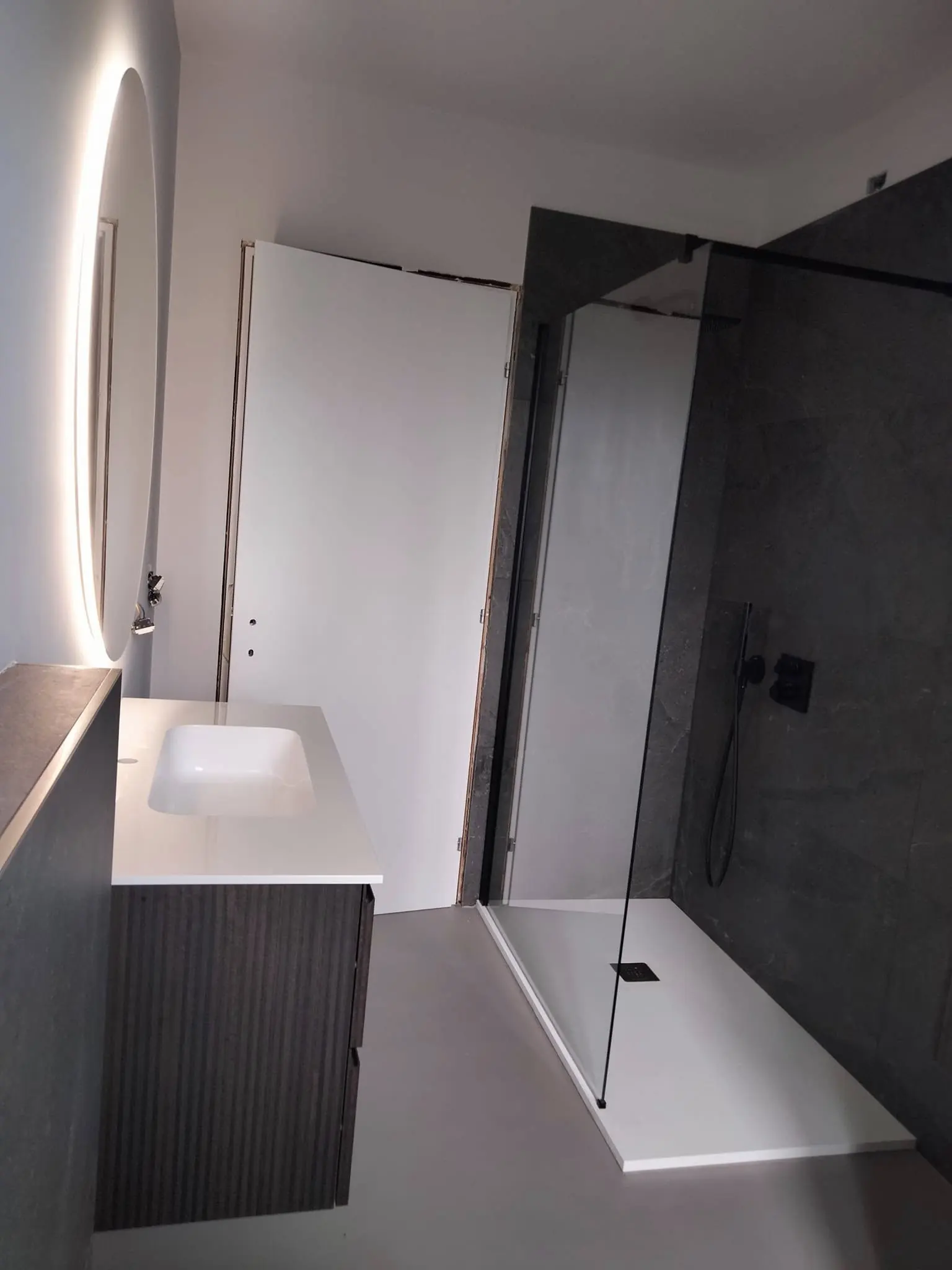 Bagno con doccia in vetro, mobile scuro e specchio retroilluminato