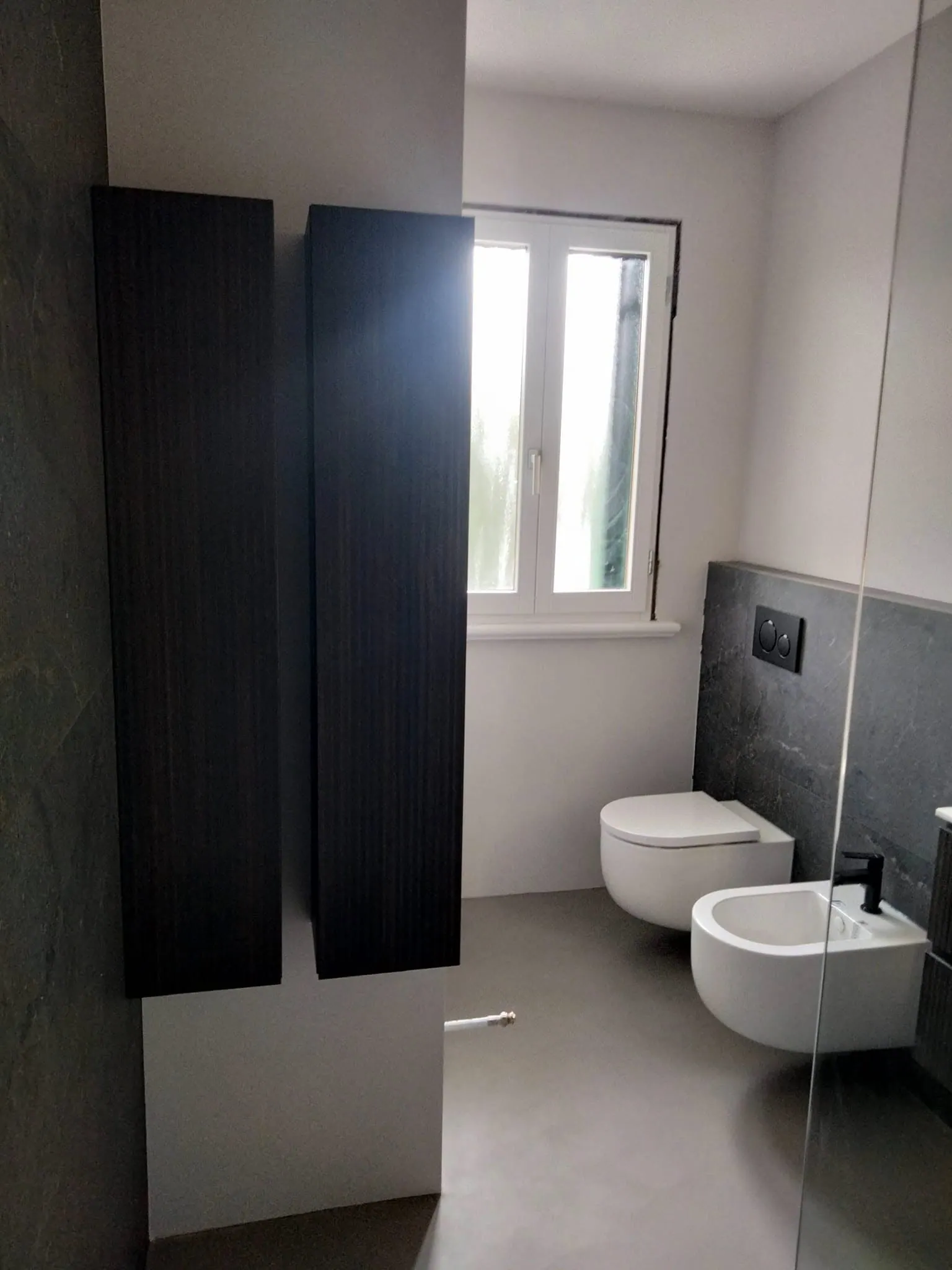 Bagno con colonne scure, sanitari sospesi e finestra