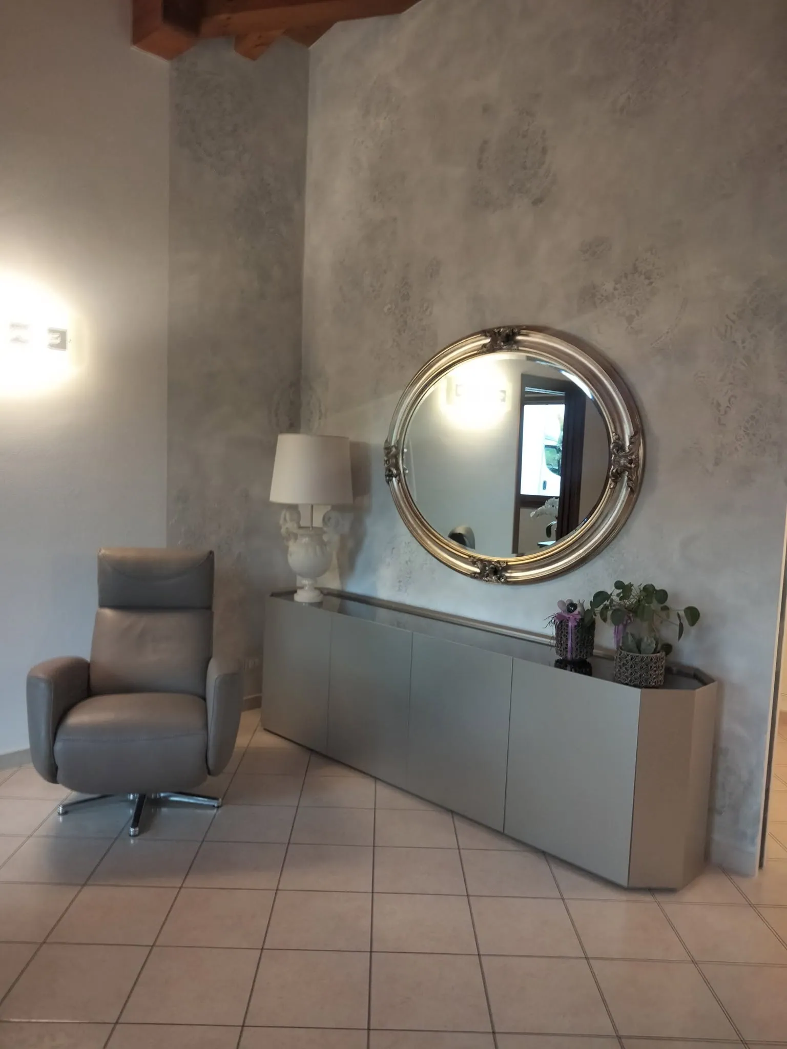 Ingresso con madia, specchio tondo e parete materica