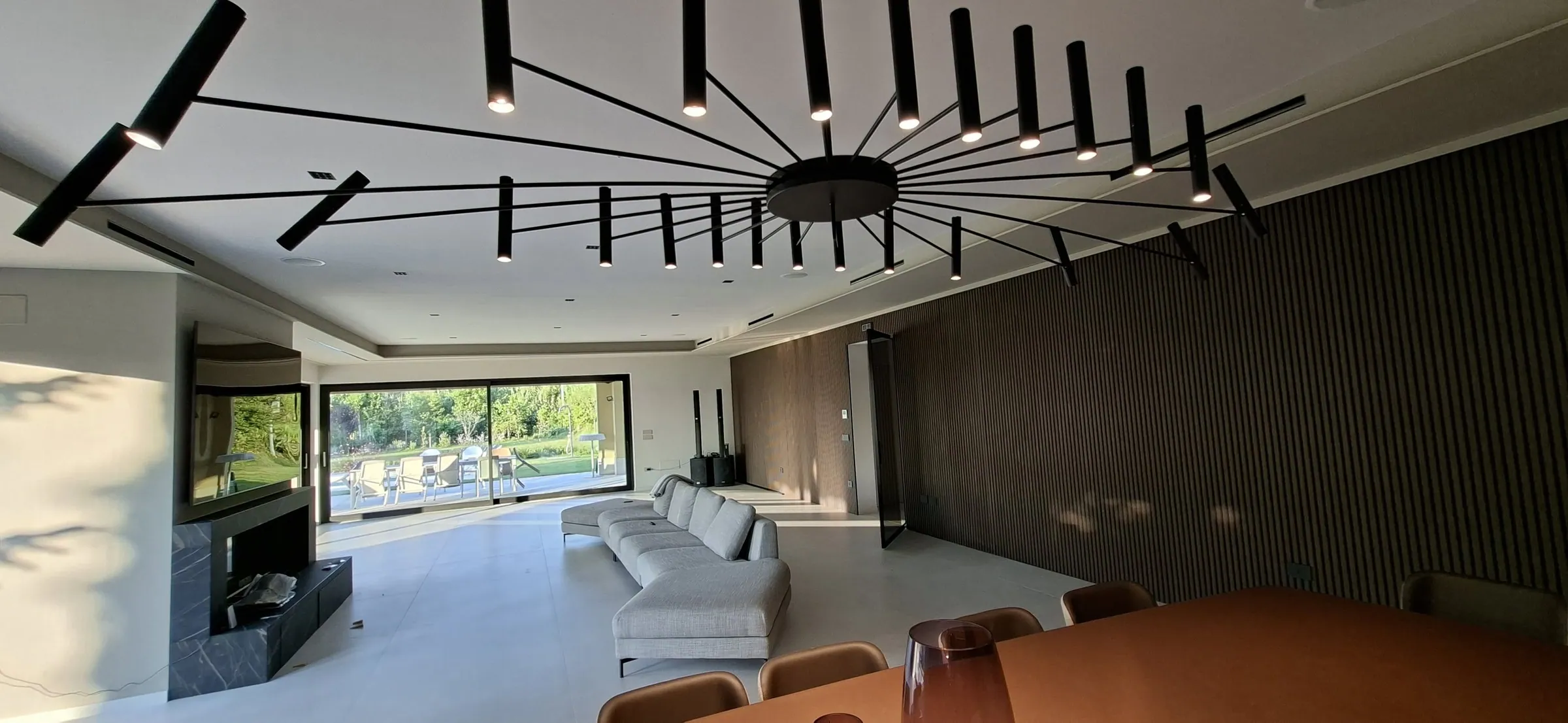 Zona giorno di una villa con lampadario a raggiera e parete in legno cannettato