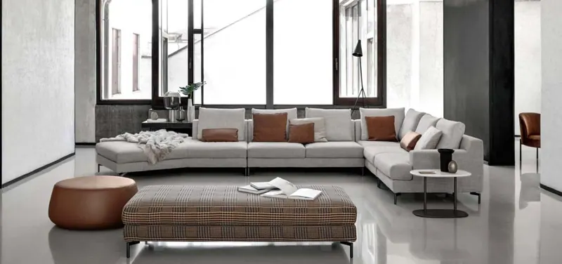 Render 3D di un loft luminoso con divano angolare chiaro, pouf in cuoio e grandi vetrate